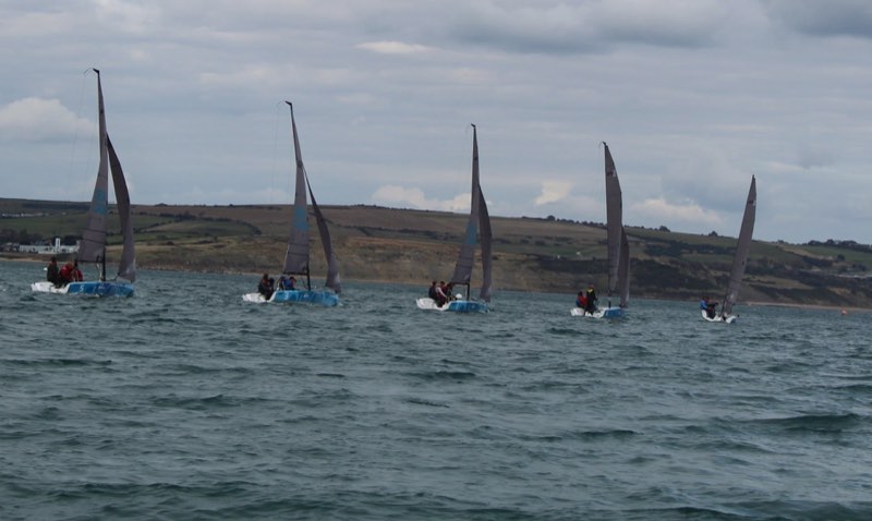 Five boats from our fleet spread across the frame on the same point of sail, the Dorset coast and a long chalk headland behind them.