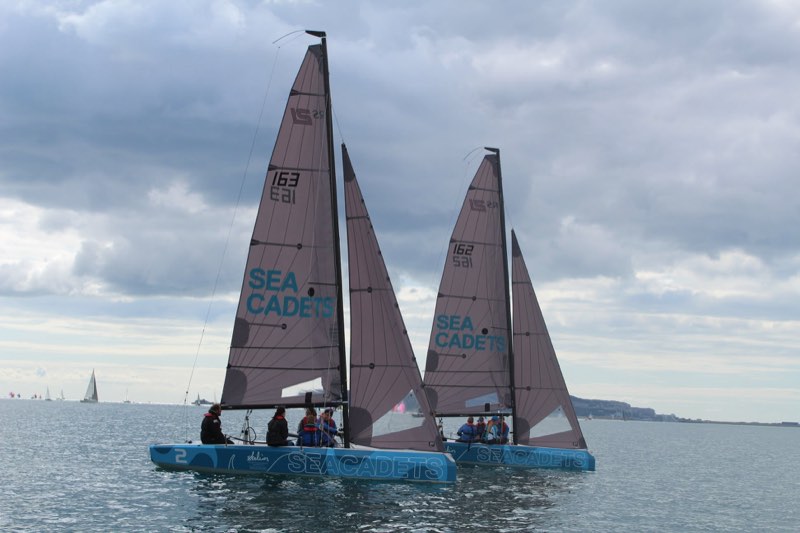 Our 163 and 162 sailing side by side under grey cloud with the Portland breakwater and other yachts in the distance.