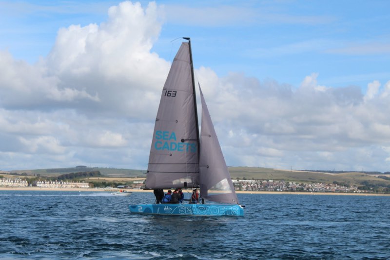 Us reaching across Weymouth Bay in bright sun, Preston beach and the ridge of hills behind, a powerboat crossing astern.