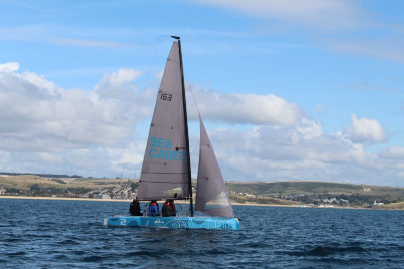 Our 163 sailing upwind under mainsail and jib with four of us sitting out, the long sweep of Weymouth Bay behind.