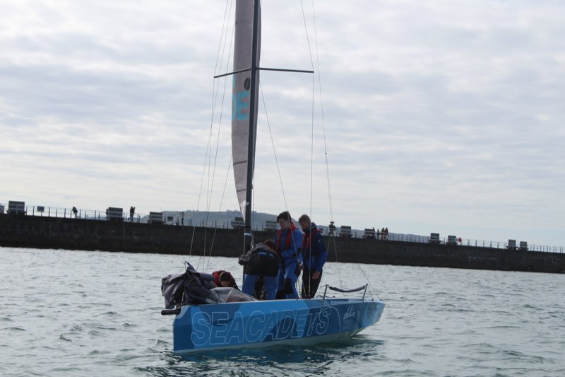 Our RS21 with sails part stowed, motoring inside the Weymouth stone pier, anglers along the pier rail and Portland rising in the distance.
