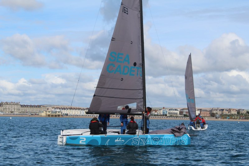Us working on the rig of 163 with the mainsail flogging, the Georgian terraces of Weymouth Esplanade along the shore behind.